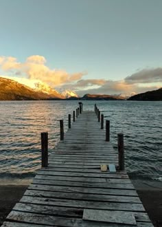 a wooden dock sitting on the side of a lake under a cloudy sky with mountains in the background