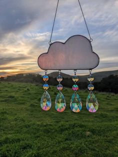 a wind chime hanging from a chain on top of a grass covered field next to a cloudy sky