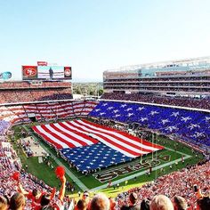 an american flag is being displayed in the middle of a football stadium as fans look on