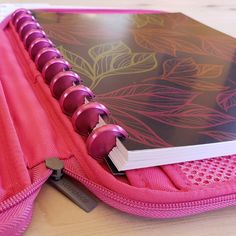 an open pink notebook on top of a pink bag with purple trim and silver accents