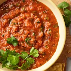 a white bowl filled with salsa and cilantro on top of tortilla chips