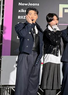 two men and a woman standing next to each other in front of a stage with microphones