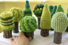 crocheted trees are displayed on a white tablecloth with a person's hand reaching for them