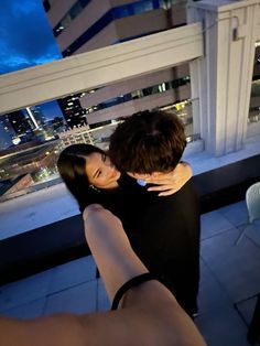 two people standing next to each other on top of a building with city lights in the background