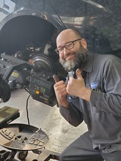 a man holding a camera and giving the thumbs up sign in front of a vehicle