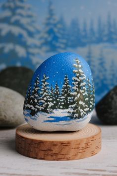 a painted rock sitting on top of a wooden stand next to rocks and snow covered trees