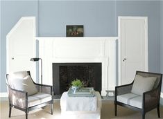 two chairs and a table in front of a fireplace with blue paint on the walls