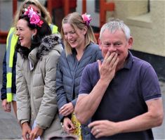 a group of people standing next to each other on a street with one woman covering her mouth