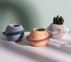 three ceramic pots with plants in them on a white counter top, one has a face drawn on it