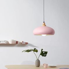 a pink lamp hanging over a wooden table with plates and cups on the shelf next to it