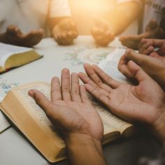 several people are sitting at a table with open books and praying hands on top of an open book