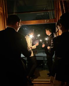 three people standing in front of a window holding sparklers and looking at each other