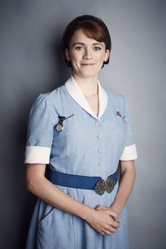 a woman in a blue dress with buttons on her lap posing for a photo against a gray background