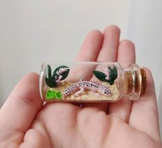 a hand holding a tiny glass bottle filled with sand and sea animals in the ocean