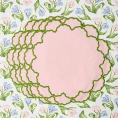 four pink and green placemats sitting on top of a white tablecloth with flowers