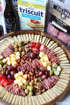 a platter filled with fruit, nuts and crackers next to bottles of wine