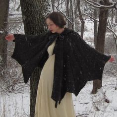 a woman in a white dress and black shawl standing next to a tree with snow falling on it