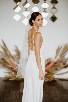 a woman in a white wedding dress with a veil on her head and flowers behind her back