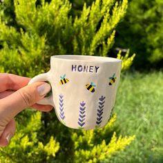 a hand holding a coffee cup with bees on it and the words honey painted on it