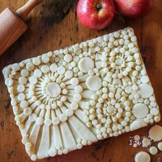 an apple pie with white frosting on a wooden table next to two apples and a rolling pin