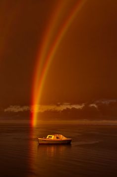 a boat in the water with a rainbow in the sky above it and a red light at the end