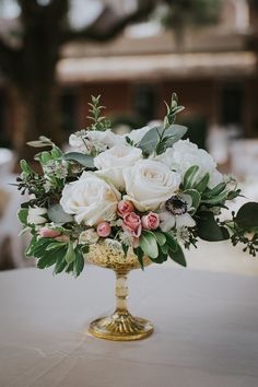 a gold vase filled with white and pink flowers on top of a table covered in greenery