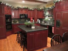 a kitchen with red cabinets and black counter tops is decorated for the holiday season, along with christmas lights