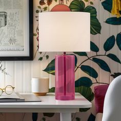 a pink lamp sitting on top of a table next to a white cup and glasses