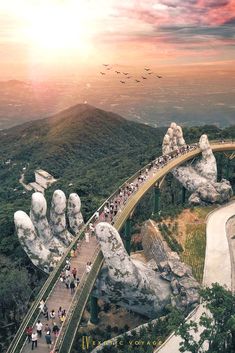 many people are walking on a bridge over some rocks in the mountains with birds flying overhead