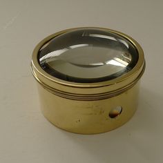 an antique brass box with a magnifying glass on the top, sitting on a white surface