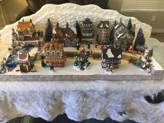 a table topped with lots of small christmas village figurines on top of snow covered ground