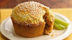 a white plate topped with a muffin covered in sesame seeds next to a green celery