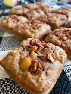 several pieces of fruit and nut muffins on a tablecloth with an apple in the background