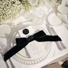 the table is set with white flowers and black ribbon, silverware, and napkins