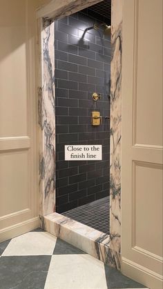 an open door leading into a bathroom with black and white tiles on the walls, along with a sign that reads close to the finish line