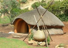 an african hut with thatched roof and grass walls, surrounded by rocks and greenery