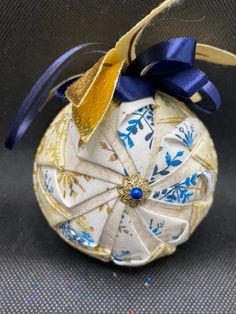 a white ornament with blue and gold designs on it's side, hanging from a ribbon