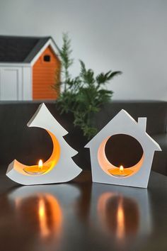 two lit candles sitting on top of a table next to a house shaped candle holder