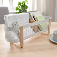 a wooden table topped with a cup and saucer next to a tray filled with napkins