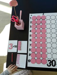 a child is making a number puzzle with pink and white circles on black paper,