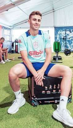 a man sitting on top of a box in the grass with his legs crossed and feet crossed