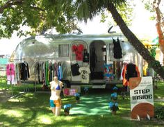 an rv parked in the grass with clothes hanging from it's roof and two mannequins standing next to it