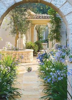 an archway leading into a garden with blue flowers