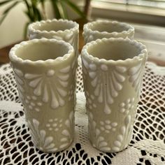 two white vases sitting on top of a doily