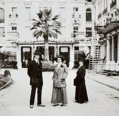 three people standing in front of a large building with palm trees on the side walk