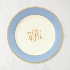 a blue and white plate with a gold monogrammed initial on the side, sitting on a marble surface