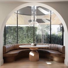 a round table with two benches underneath it in front of an arched window that overlooks the garden