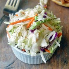 a bowl filled with coleslaw sitting on top of a wooden table next to a fork