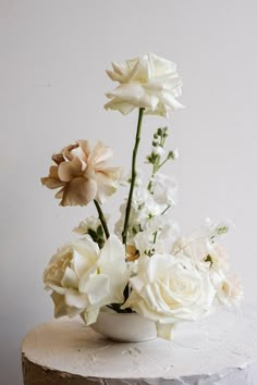 a white flower arrangement in a vase on a table with a white wall behind it