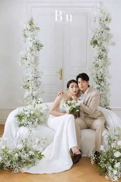 the bride and groom are sitting on a white couch in front of an archway with greenery